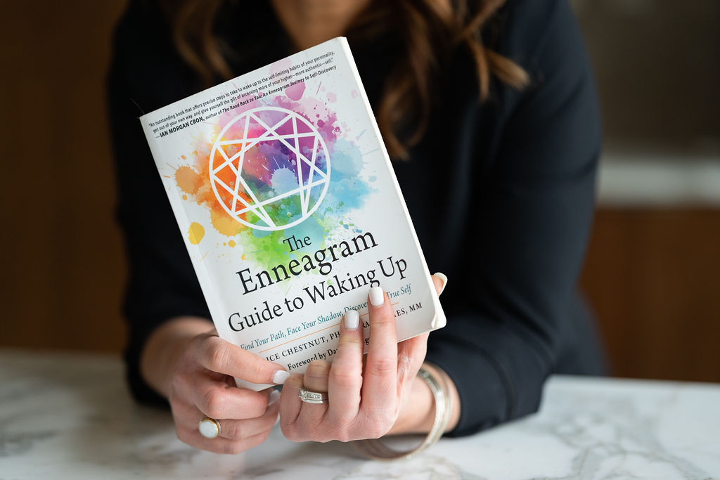 Jennifer is holding The Enneagram Guide to Waking Up. This one of the many resources Jennifer uses to help guide you to your Enneagram Personality Type - YOUR number.