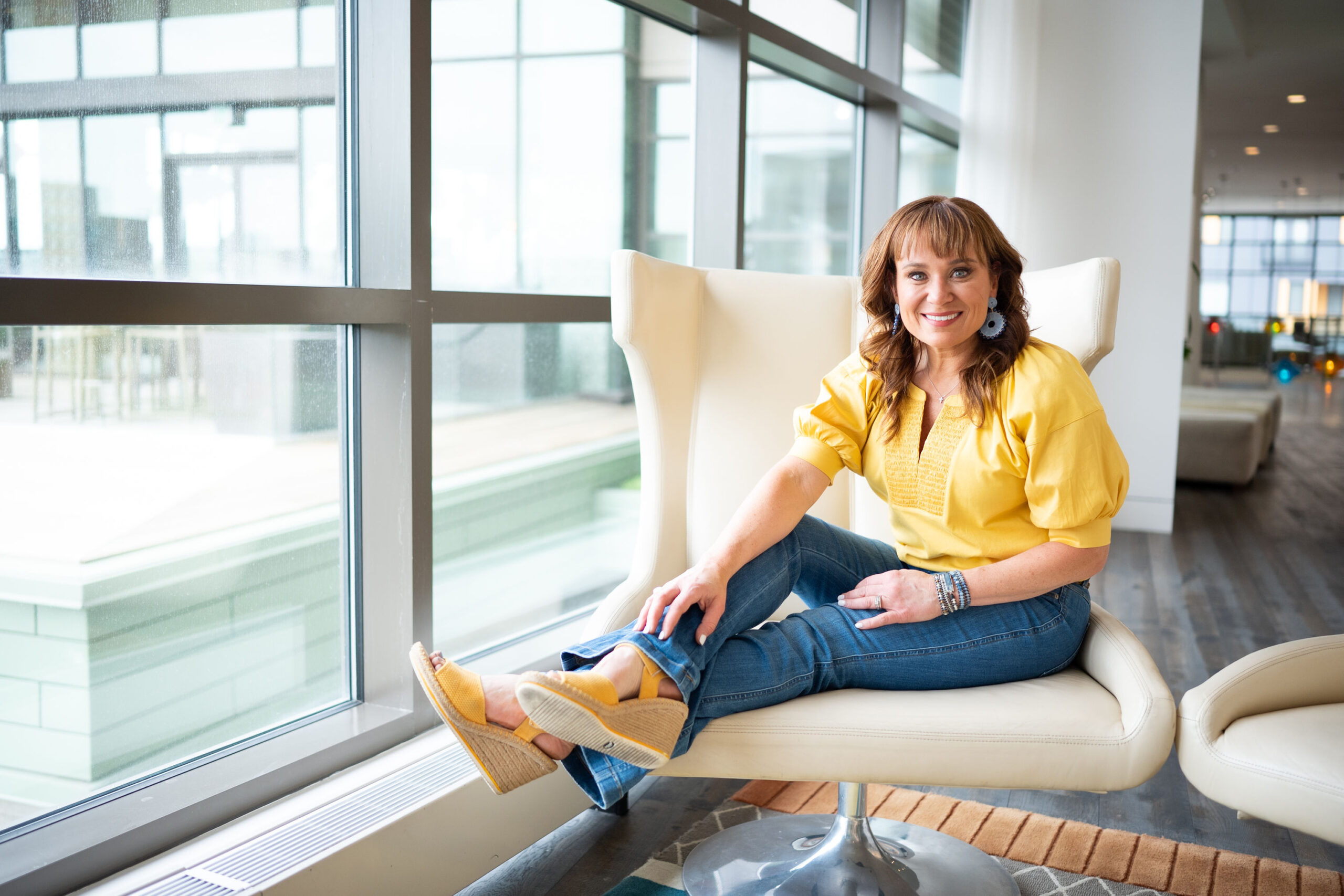 Jennifer wearing a cheerful yellow shirt, sitting in front of a window.